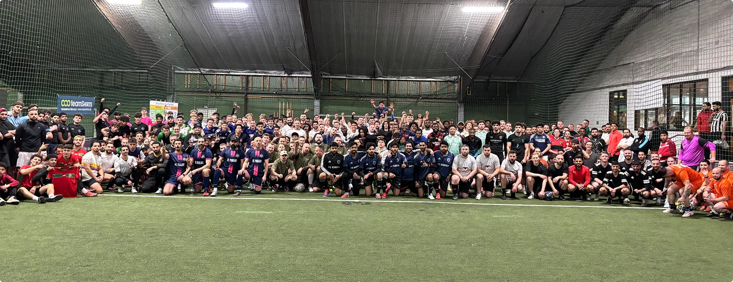 Panorama-Gruppenfoto aller Teams beim JUGAD x TeamShirts Cup Köln, links ein TeamShirts-Banner am Spielfeldrand