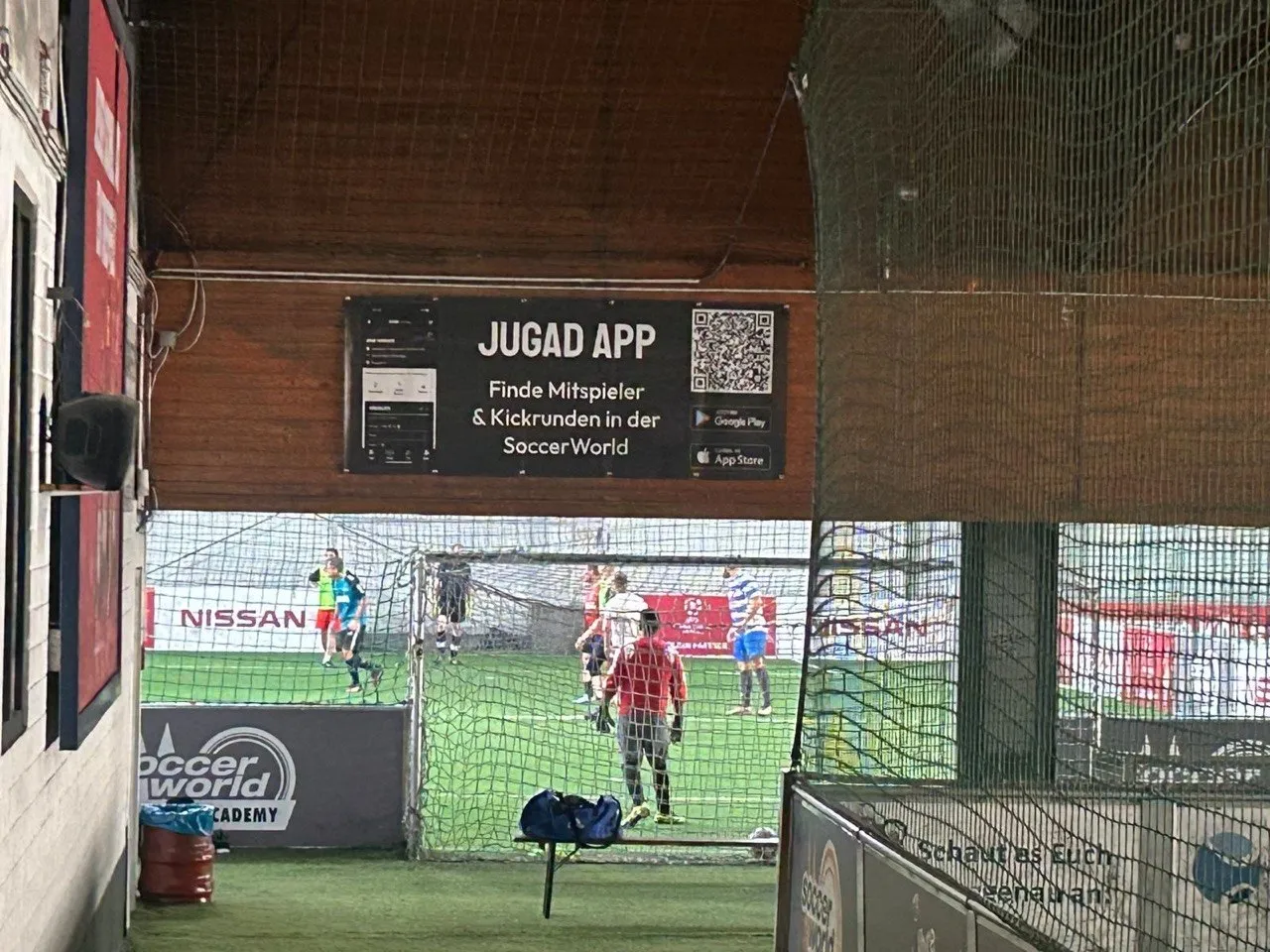 JUGAD-Banner „Finde Mitspieler & Kickrunden“ über einem Spielfeld in einer Soccerhalle